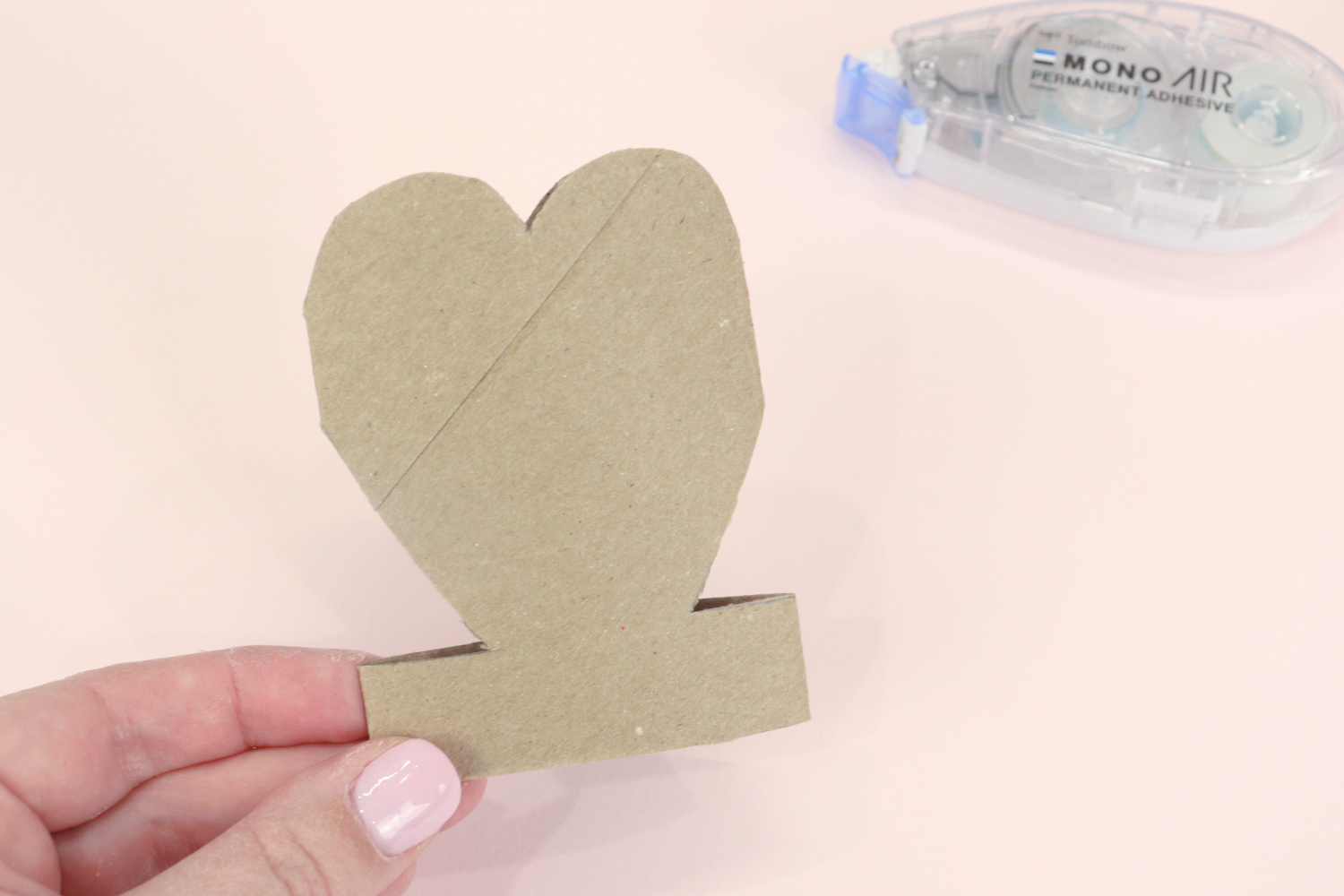 Image contains Amy’s hand holding a heart shape cut from a toilet paper roll. An adhesive runner sits behind it on a pink background.