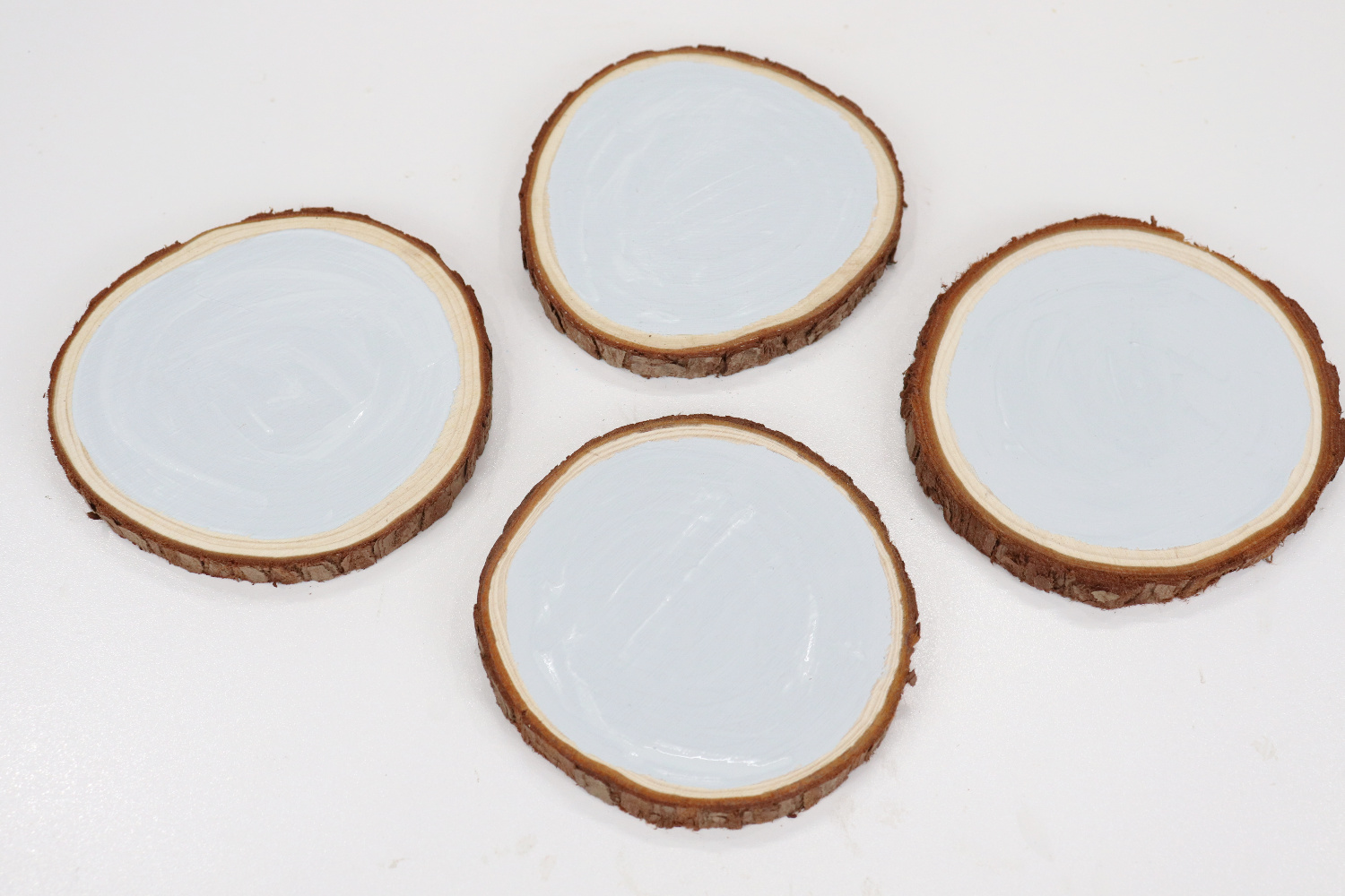 Image contains four small wood slices painted with a light gray chalk paint.