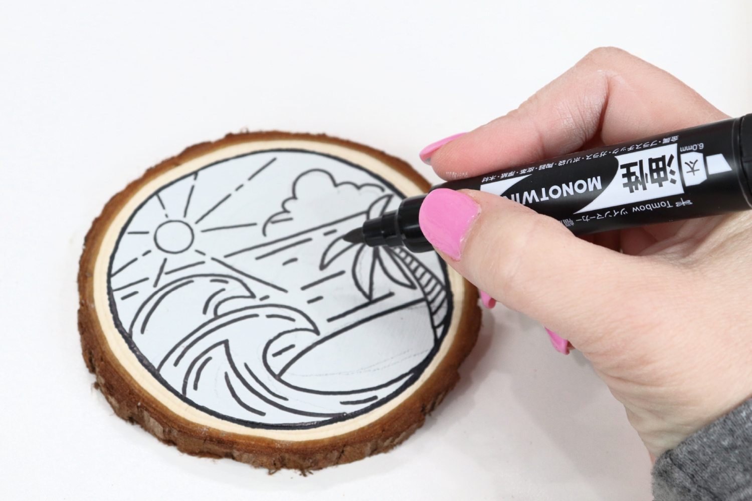 Image contains Amy’s hand holding a black MONOTwin marker and drawing on a painted wood slice.