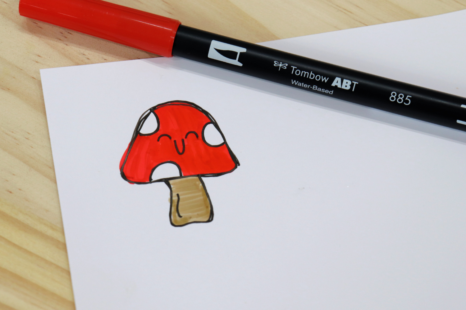 Image contains a red and white toadstool doodled on a piece of white vinyl. A red Dual Brush Pen sits nearby on a wooden background.