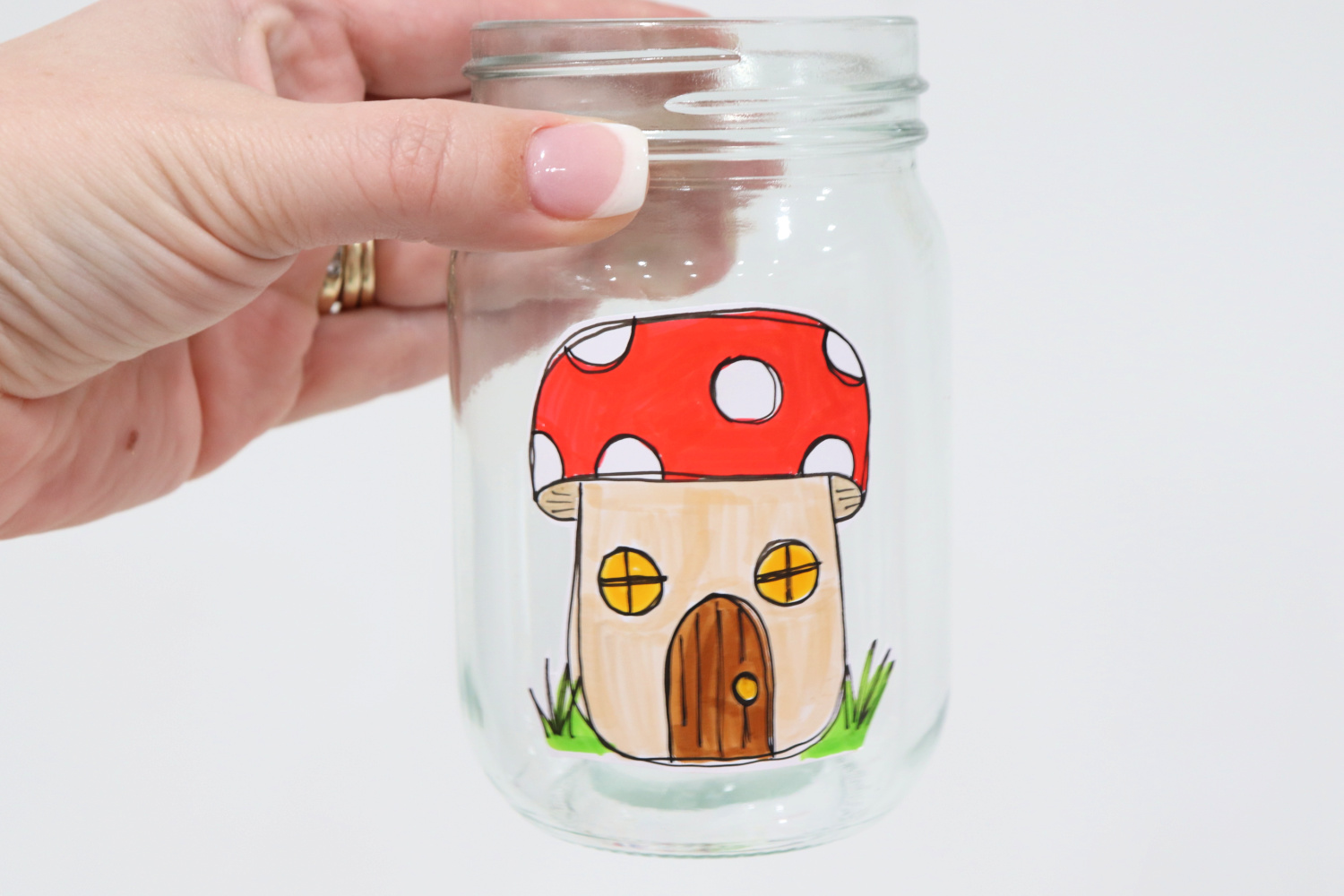 Image contains Amy’s hand holding a mason jar with a toadstool house sticker applied to the front center area.