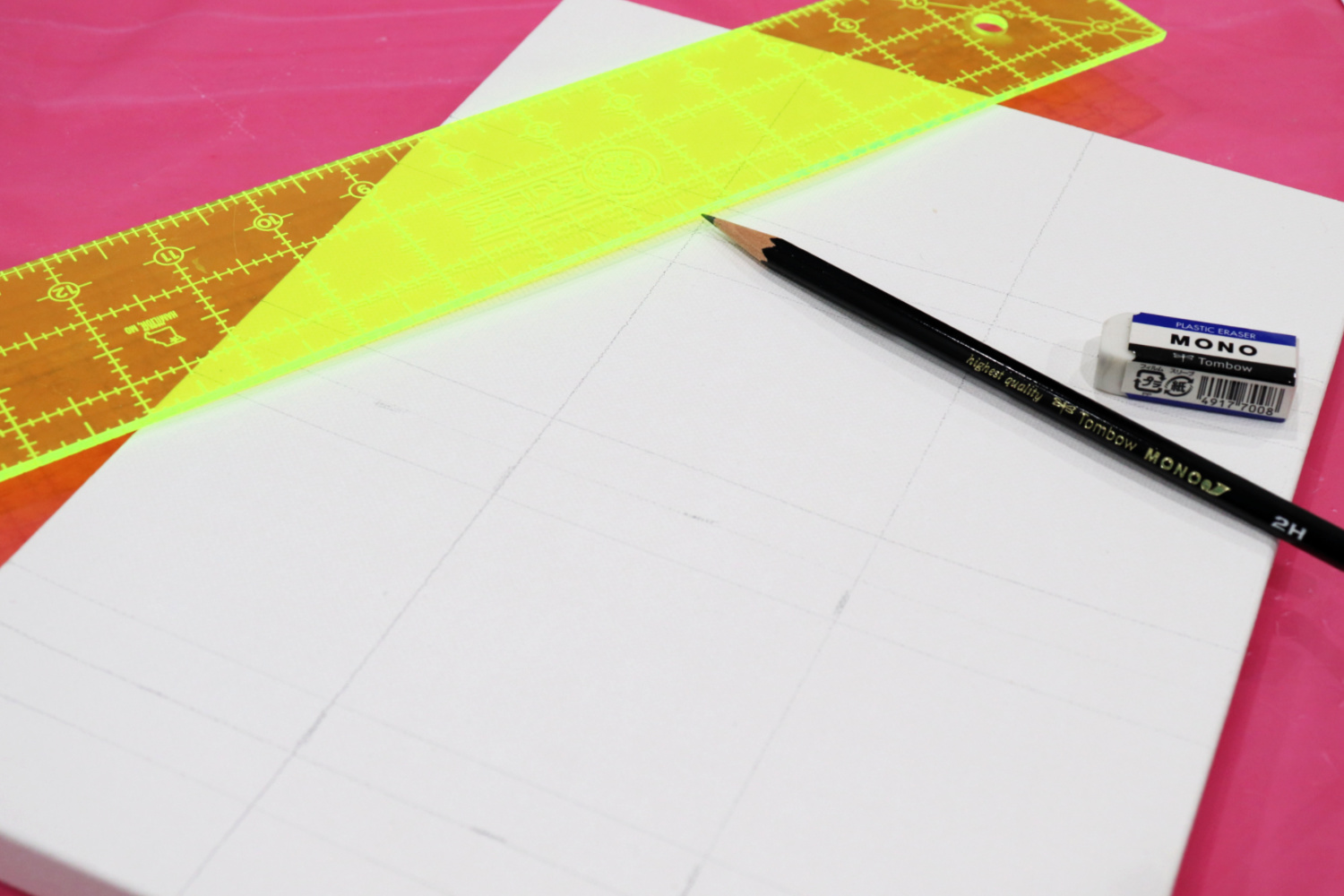 Image contains a white canvas with a black pencil, white eraser, and bright yellow ruler on top. The canvas is divided into sections with light pencil lines.