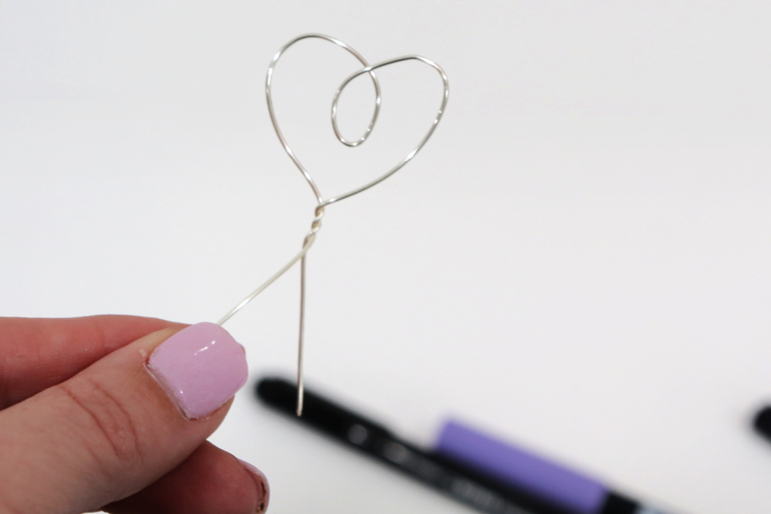 Image contains Amy’s hand holding silver wire that has been twisted into a loopy heart.