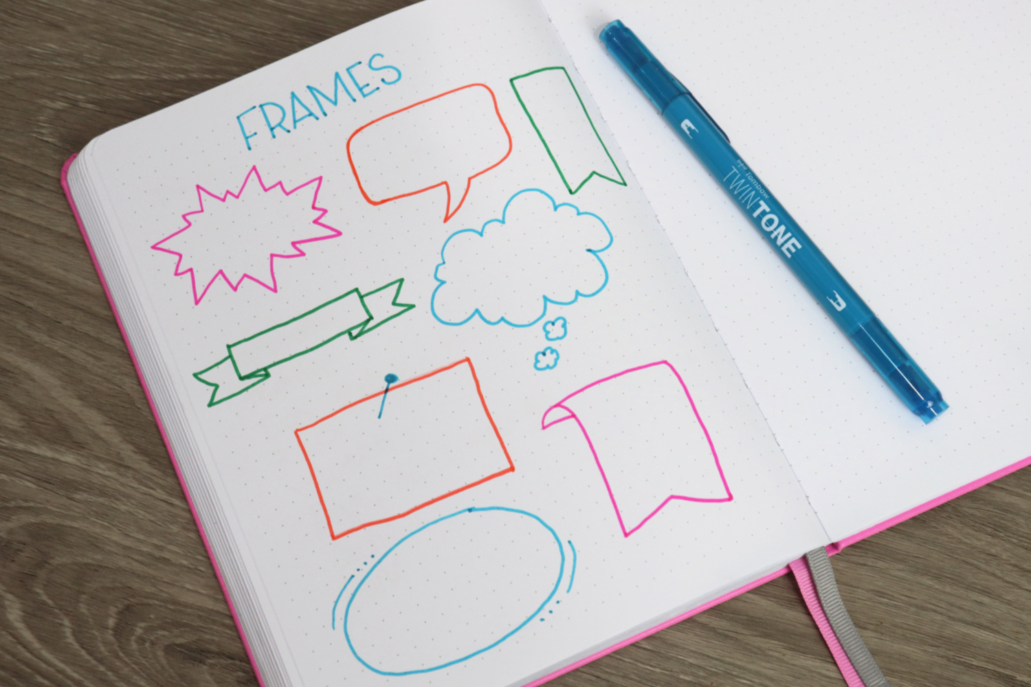 Image contains an open notebook with a variety of colorful shapes drawn on the left page. A blue marker sits to the side.