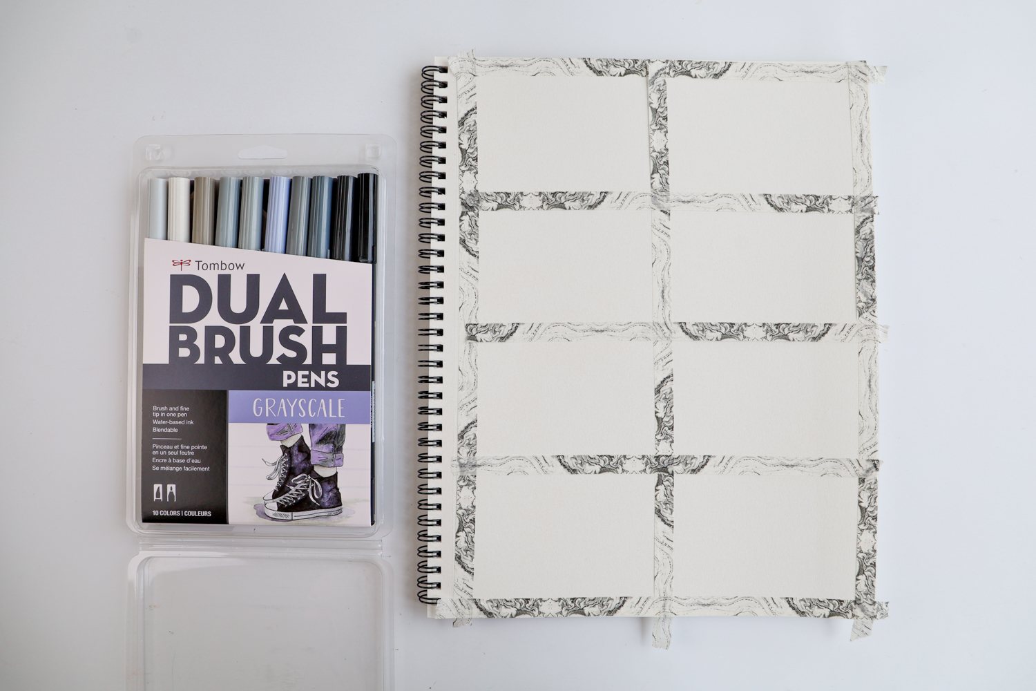 Tombow Grayscale Dual Brush Pen 10-pack laying next to a sketchbook