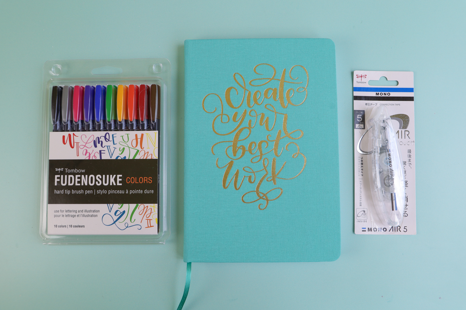 Tombow Fudenosuke Color Brush Pens, Bullet Journal, and MONO Air Correction Tape laying on a blue background