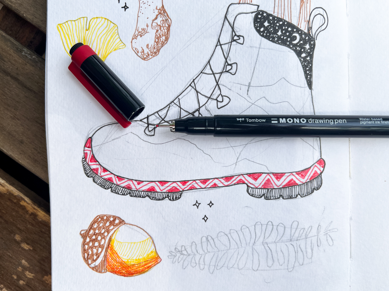 Tombow MONO Drawing Pen in Red laying on a sketchbook with a hiking boot drawing