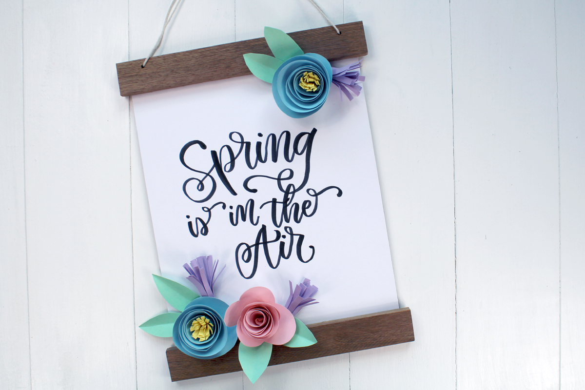 Spring Banner with hand lettering reading "Spring is in the Air" with rolled paper flowers.