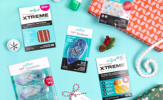 Flat lay of Tombow adhesives including Xtreme Putty, Xtreme Tabs, Adhesive Dots, MONO Multi XL Liquid Glue, and MONO Adhesive Permanent surrounded by festive wrapping supplies.
